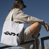Person sitting on a railing with a white tote bag featuring a logo.