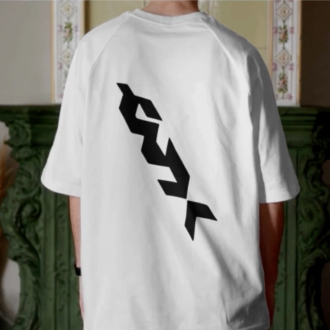 Person wearing a white t-shirt with black logo on the back, standing indoors.